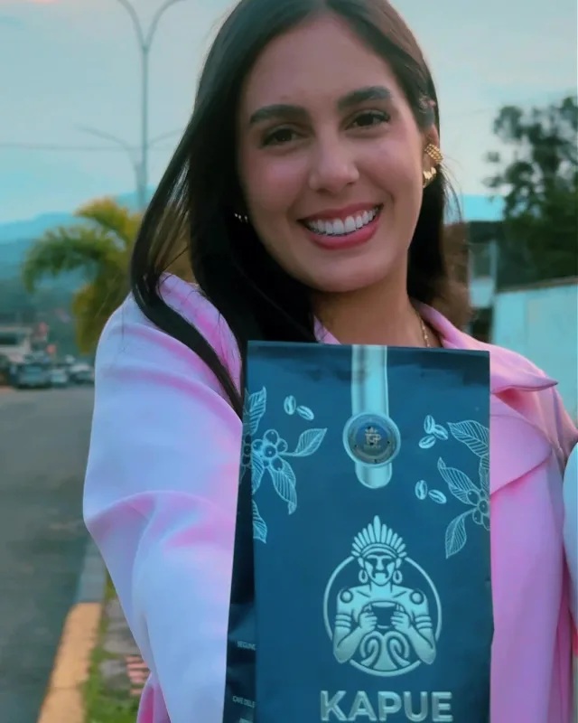 Mujer sonriendo al aire libre sostiene una bolsa azul de Kapue, con las montañas al fondo.